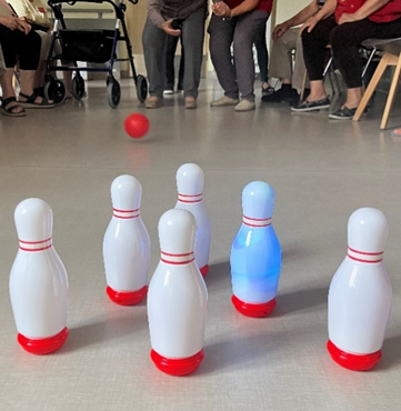 Zdjęcie_nr_2_przedstawia_mieszkańców_w_tym_osobę_rzucającą_czerwoną_kule_wycelowaną_w_ustawione_kręgle.png