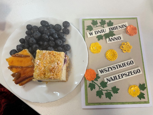 Zdjęcie_nr_6_przedstawia_własnoręcznie_przygotowana_kartka_imieninowa_oraz_talerzyk_z_borówkami_i_kawałkami_ciasta.png