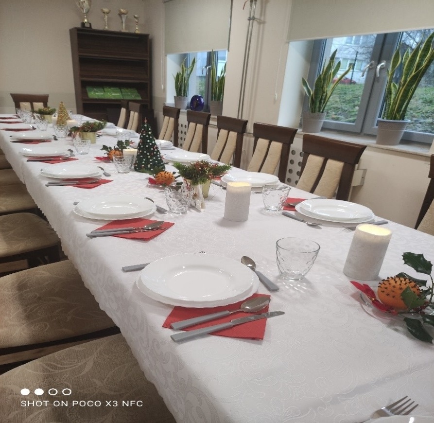  Aranżacja stołu wigilijnego z białym obrusem i dodatkami ze świątecznymi motywami. Zastawa stołowa w kolorze białym, komplet sztućców, świece, pomarańcze z goździkami, stroiki świąteczne.