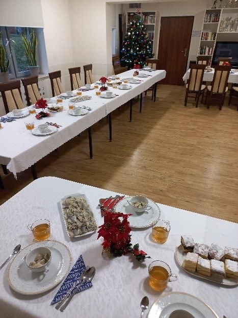 Zdjęcie. Na głównym planie mamy stół przygotowany na wigilie oraz choinkę.