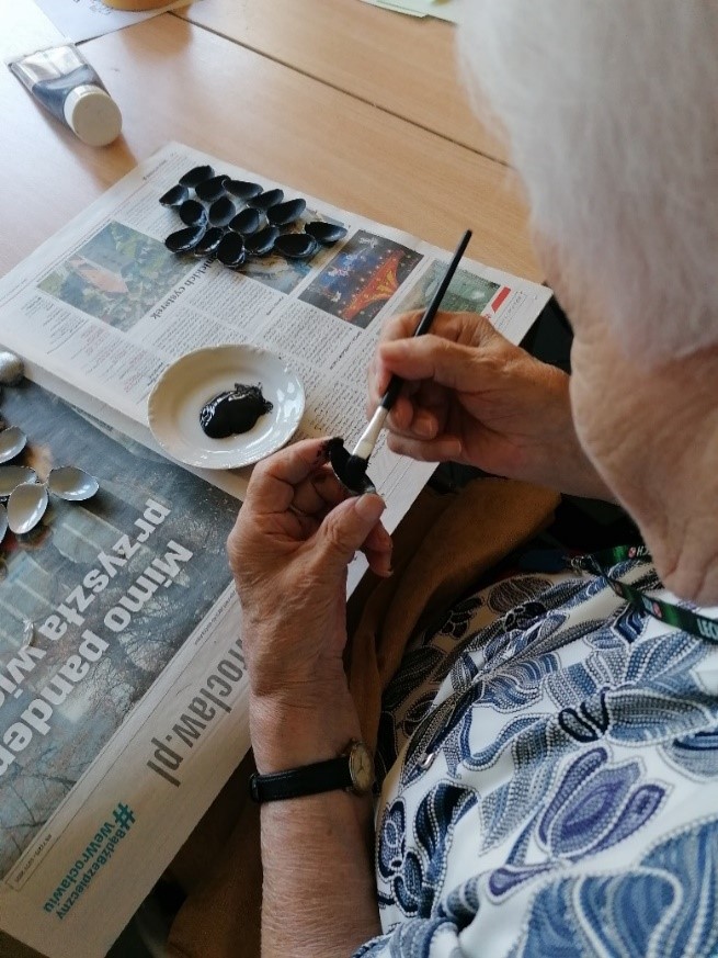 Mieszkanka siedzi w pracowni terapii zajęciowej i maluje czarną farbą łyżeczki plastikowe