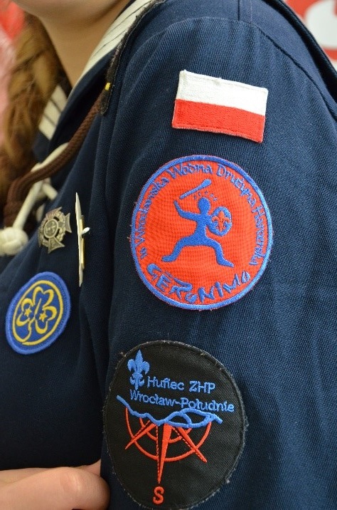 Zdjęcie 3. Ramię harcerki, na którym znajdują się emblematy: 1)flaga Polski, 2)nazwa drużyny- 16 Wrocławska Wodna Drużyna Harcerska 3)Logo- Wrocław-Południe Hufiec ZHP
