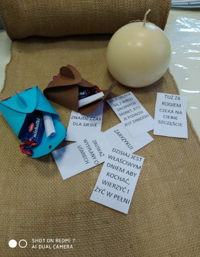 Zdjęcie ukazuje leżącą białą kule na brązowym materiale oraz białe kartki