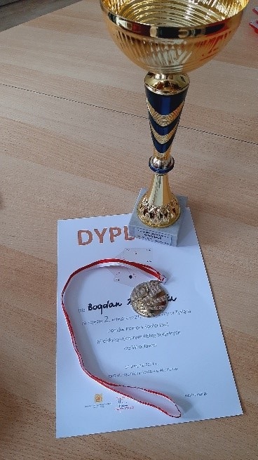 Na zdjęciu puchar oraz medal za zajęcie II miejsca w rozgrywkach w tysiąca. Tłem zdjęcia jest sosnowy stolik